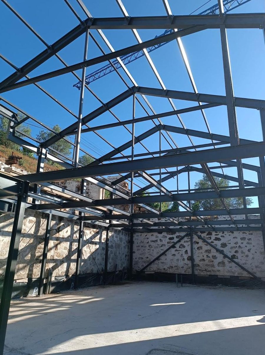 Estrutura metálica de cobertura montada sobre as paredes de pedra de um edifício em reabilitação.